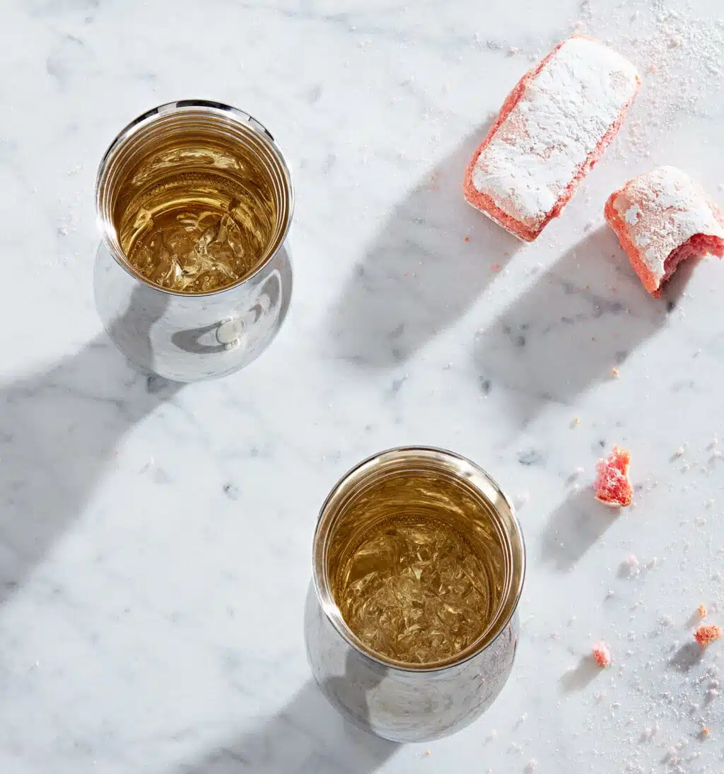 Deux timbales en argent massif de la collection Pour le champagne de Puiforcat, sur une table en marbre, photographiés à côté de pâtisseries roses