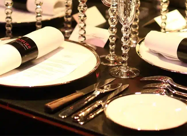 Set de couverts de table en argent massif de la collection Louvois de Puiforcat disposés sur une table dressée d'assiettes de la collection Cercle d'Orfèvre, dans le restaurant l'Atelier de Joël Robuchon