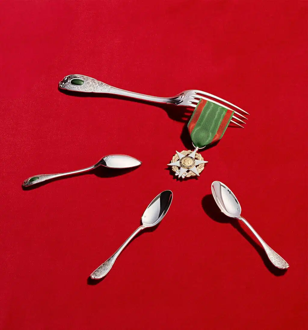 Couverts de table de la collection Elysée en argent massif et jade photographiés sur un fond rouge à côté d'une médaille en symbole de la république française