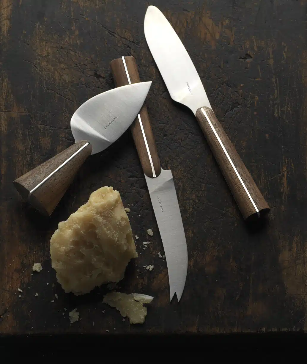 Cheese knives from Couteaux d'orfèvre collection photographed with parmesan on a brown table